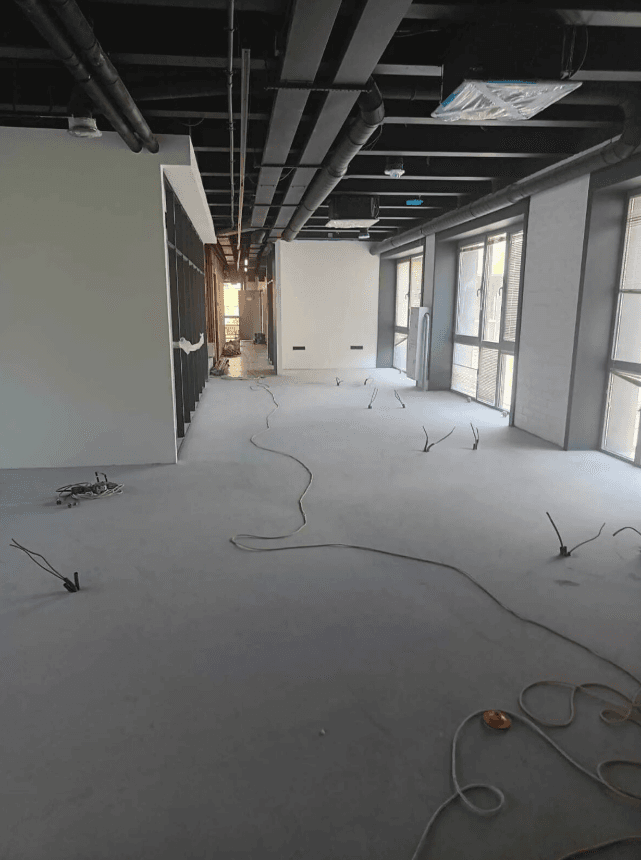 Large commercial space under construction showing exposed steel ceiling, HVAC ductwork, and open floor plan