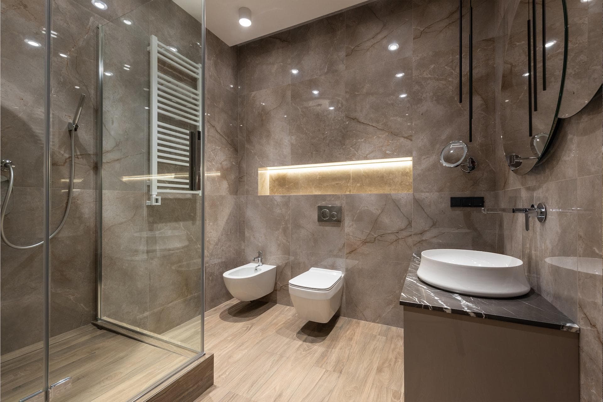 Modern luxury bathroom with large-format marble tiles, glass shower enclosure, vessel sink, and LED-lit niche